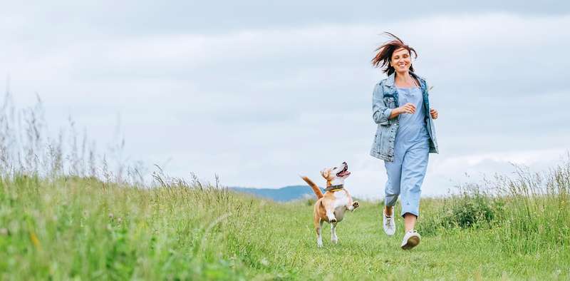 Frau und Hund rennen glücklich über Wiese